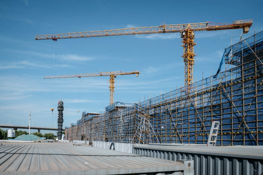 View of a construction site with yellow tower cranes and scaffolding under a clear blue sky.