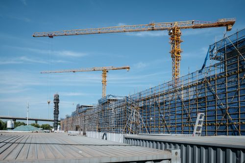 Free View of a construction site with yellow tower cranes and scaffolding under a clear blue sky. Stock Photo