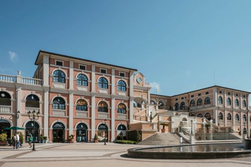 Free Beautiful Italianate shopping piazza featuring a fountain and classic architecture under a clear blue sky. Stock Photo