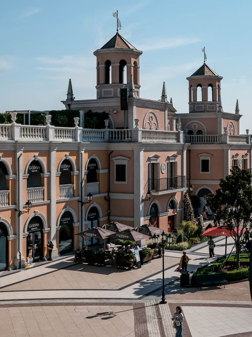 Free Elegant Italian-style shopping center with cafe umbrellas under a sunny sky. Stock Photo