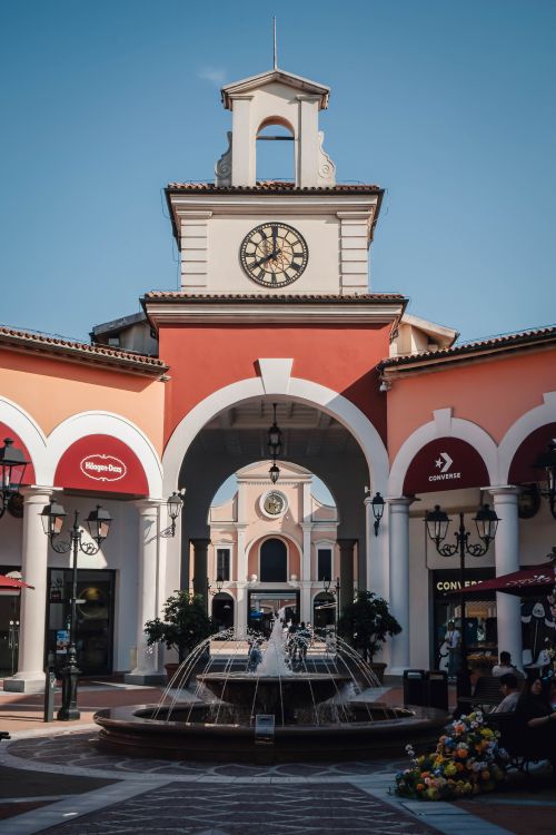 Free A vibrant outdoor shopping plaza featuring a prominent clock tower and water fountain, ideal for retail exploration. Stock Photo