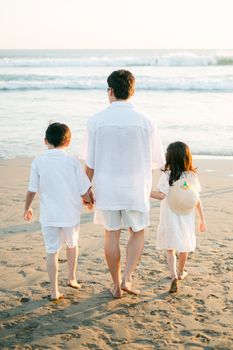 A father and children enjoy a peaceful walk by the ocean, embracing nature's beauty.