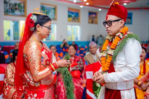 Free Bride and groom in traditional attire during an indoor Nepali wedding ceremony with guests seated. Stock Photo