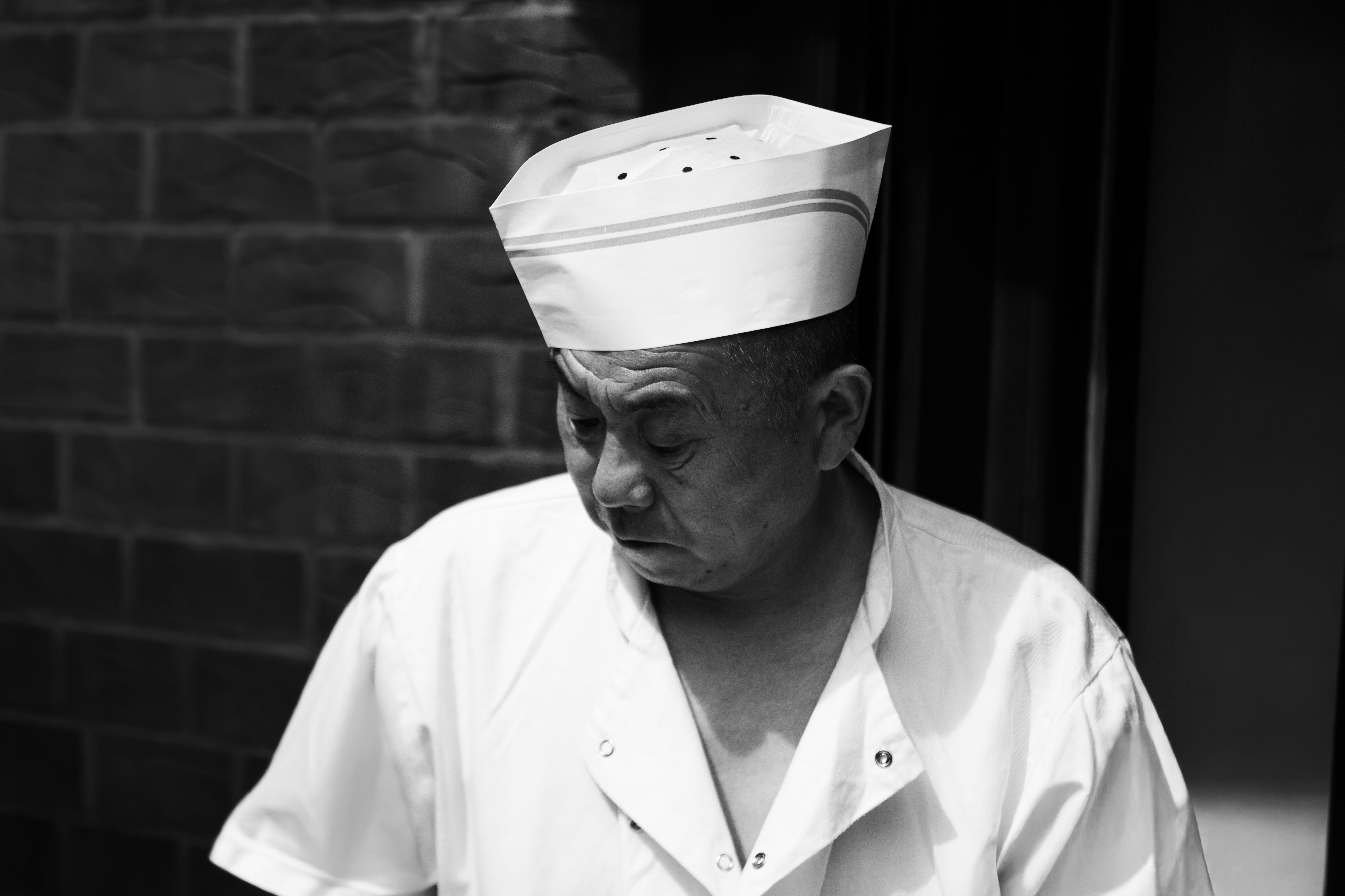 Black and white portrait of a chef in uniform, reflecting in a quiet moment.