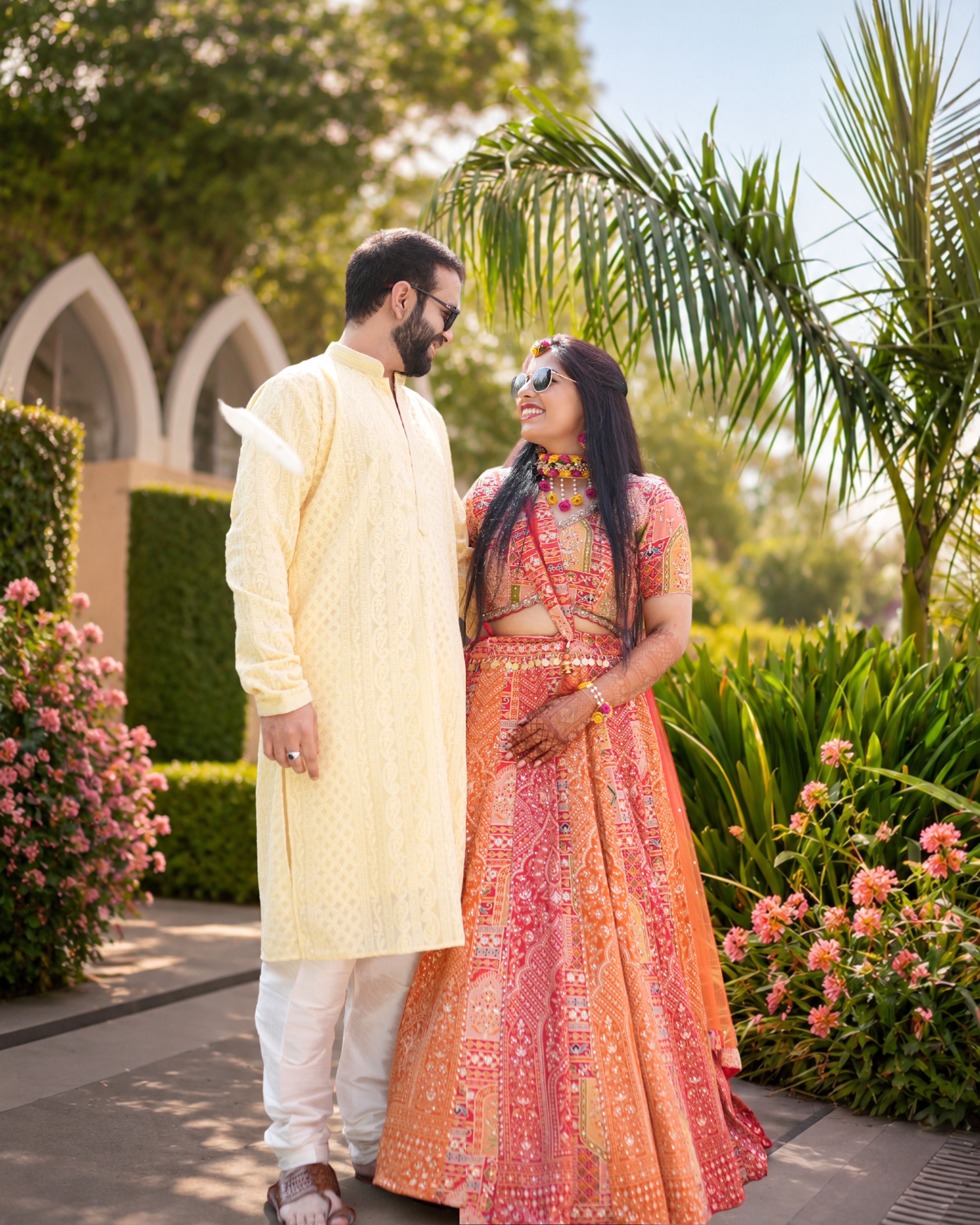 A joyful Indian couple in vibrant traditional attire during a garden wedding shoot.