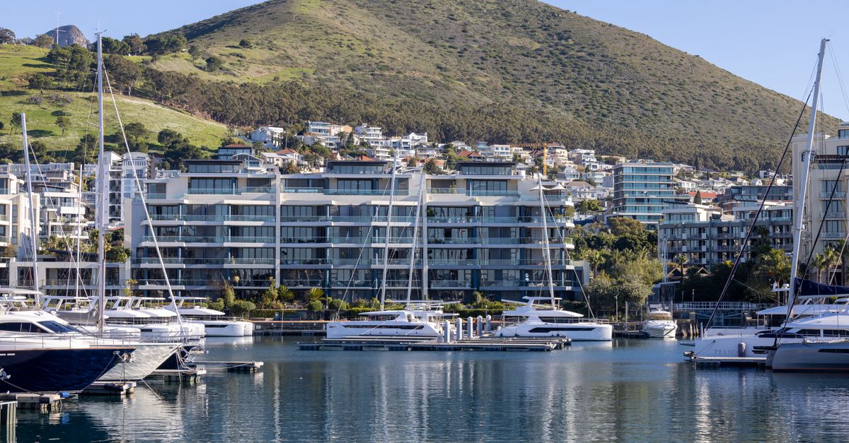 Waterfront view of luxury yachts in a scenic marina with hilly backdrop and modern apartments.