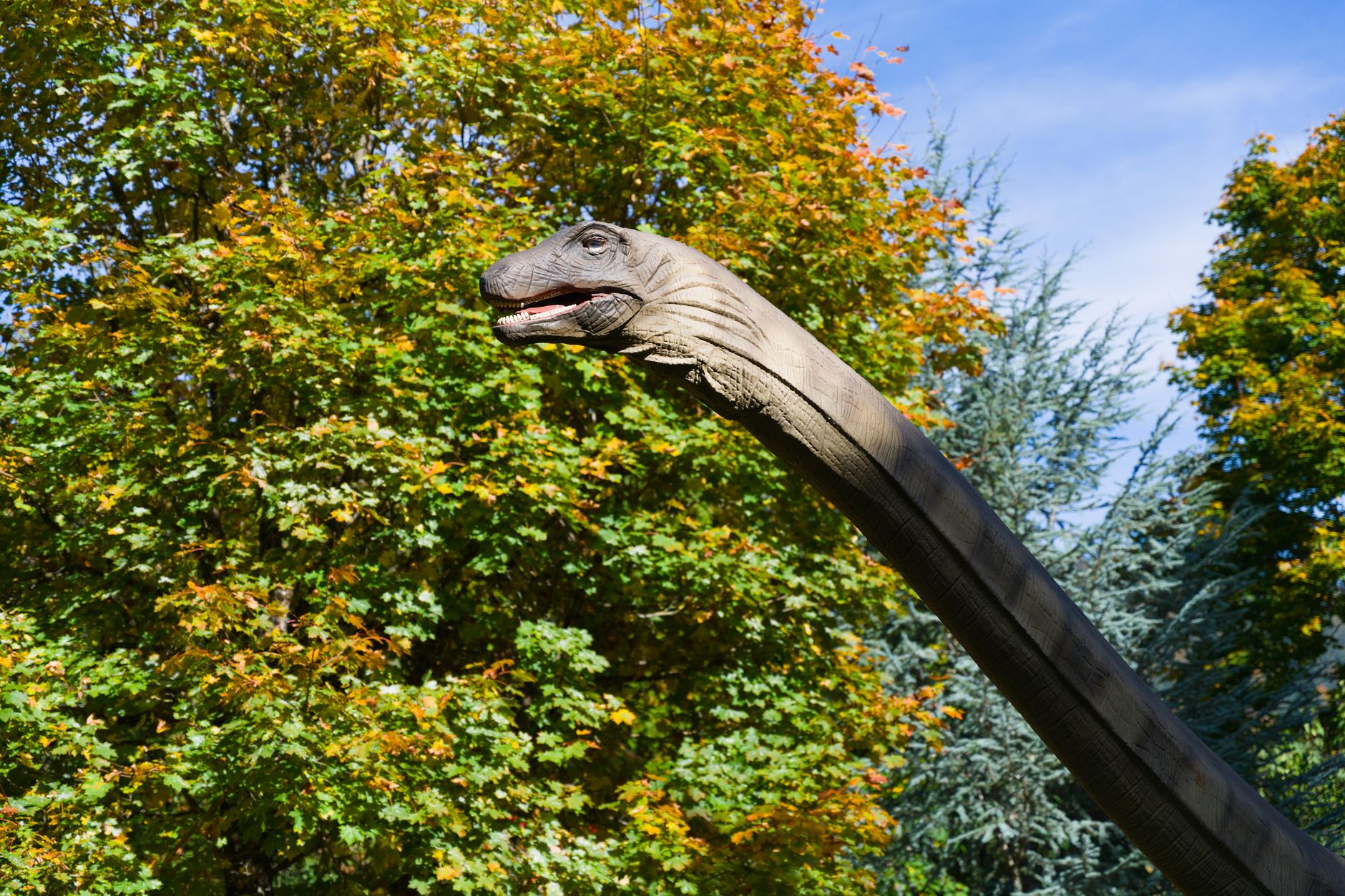 Dinosaur sculpture among vibrant autumn foliage under a clear blue sky.