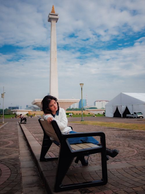Free A young woman sits by the National Monument (Monas) in Jakarta, enjoying a sunny day outdoors. Stock Photo