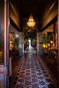 View of a vintage restaurant's elegant hallway with a grand chandelier and patterned floor tiles.