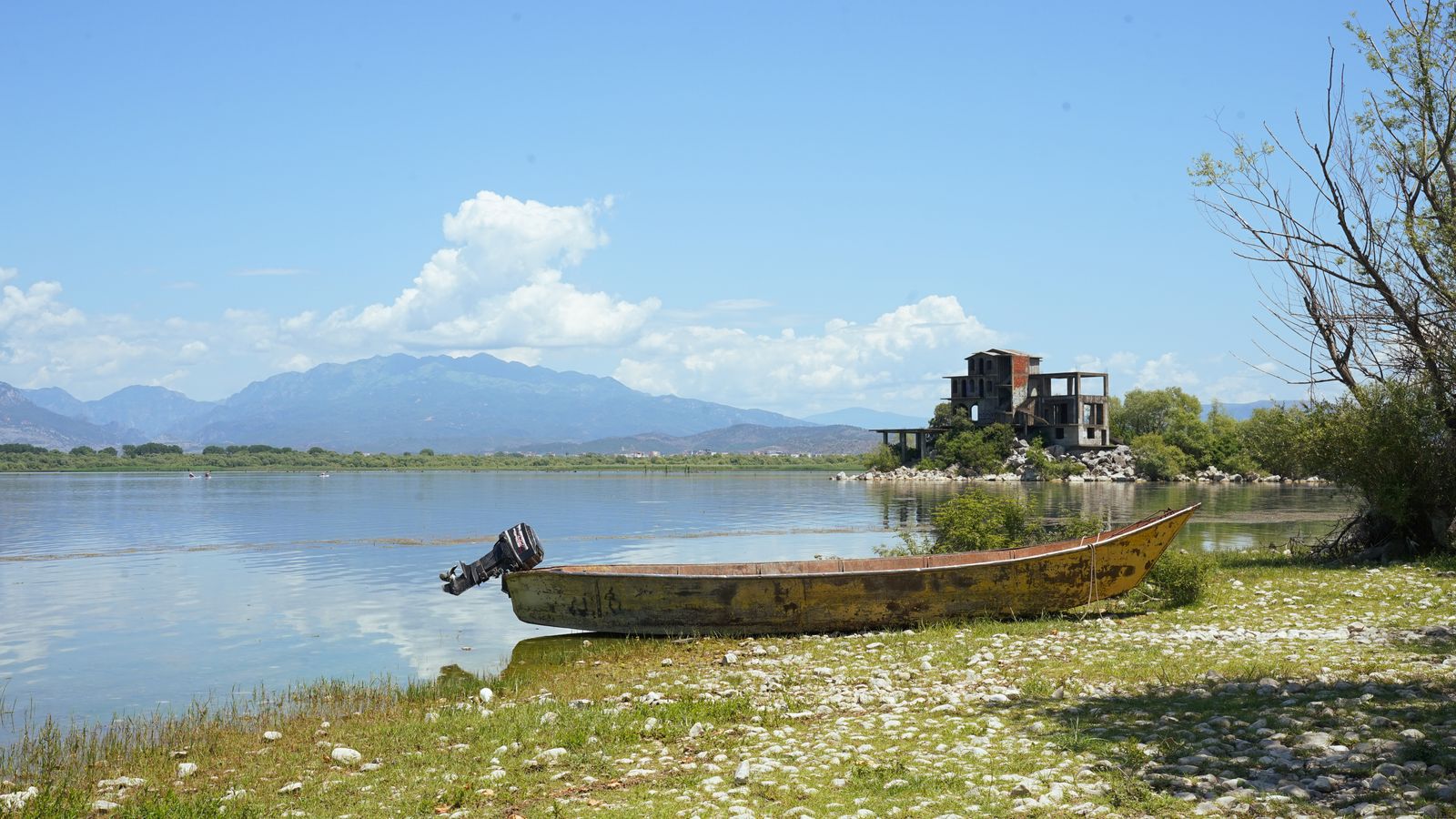 Le lac de Shkodër paisible à Shirokë, avec une vieille barque sur la rive et les montagnes au loin