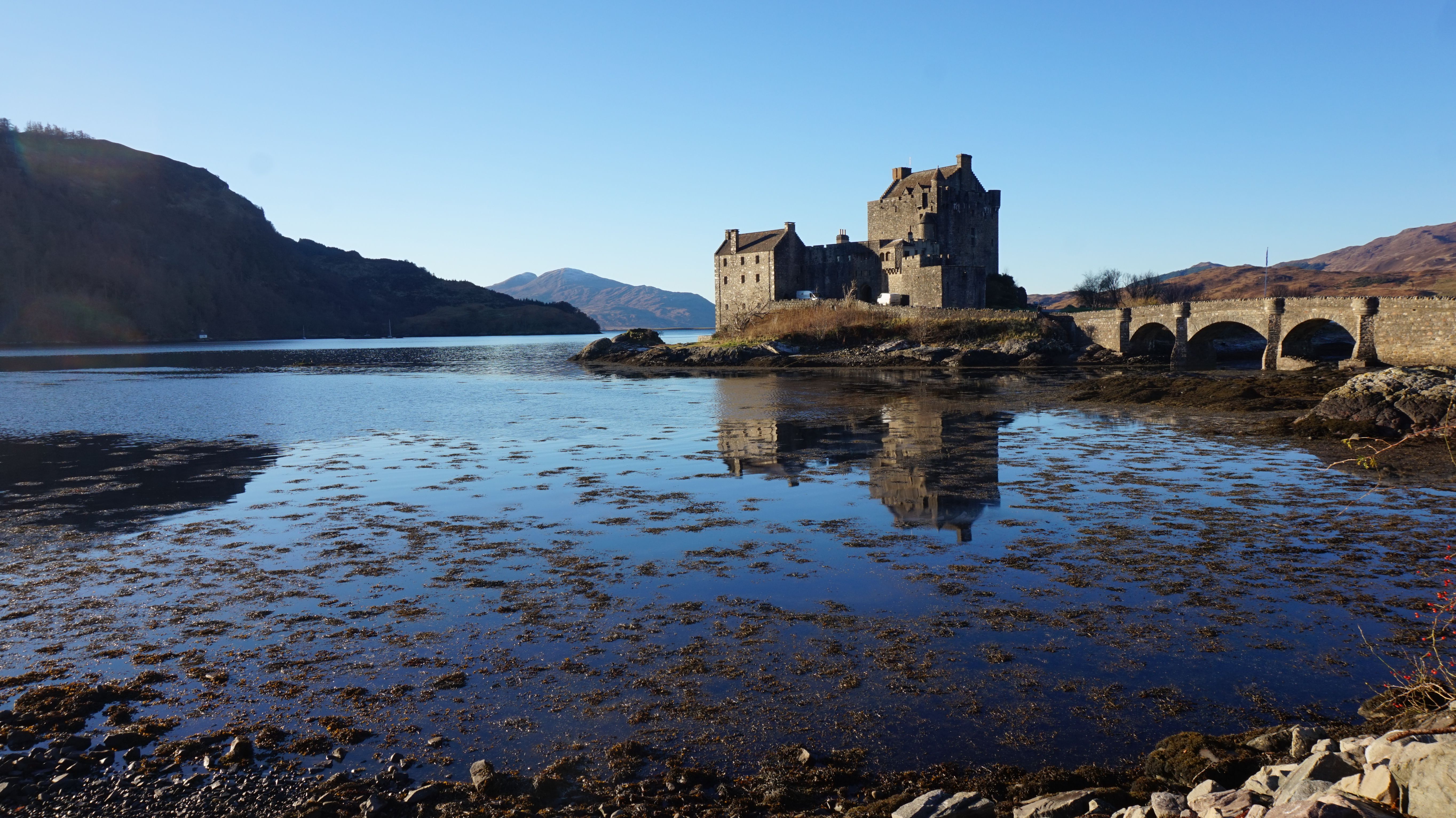 Eilean Donan Castle mirrored in a serene Scottish loch on a clear day.