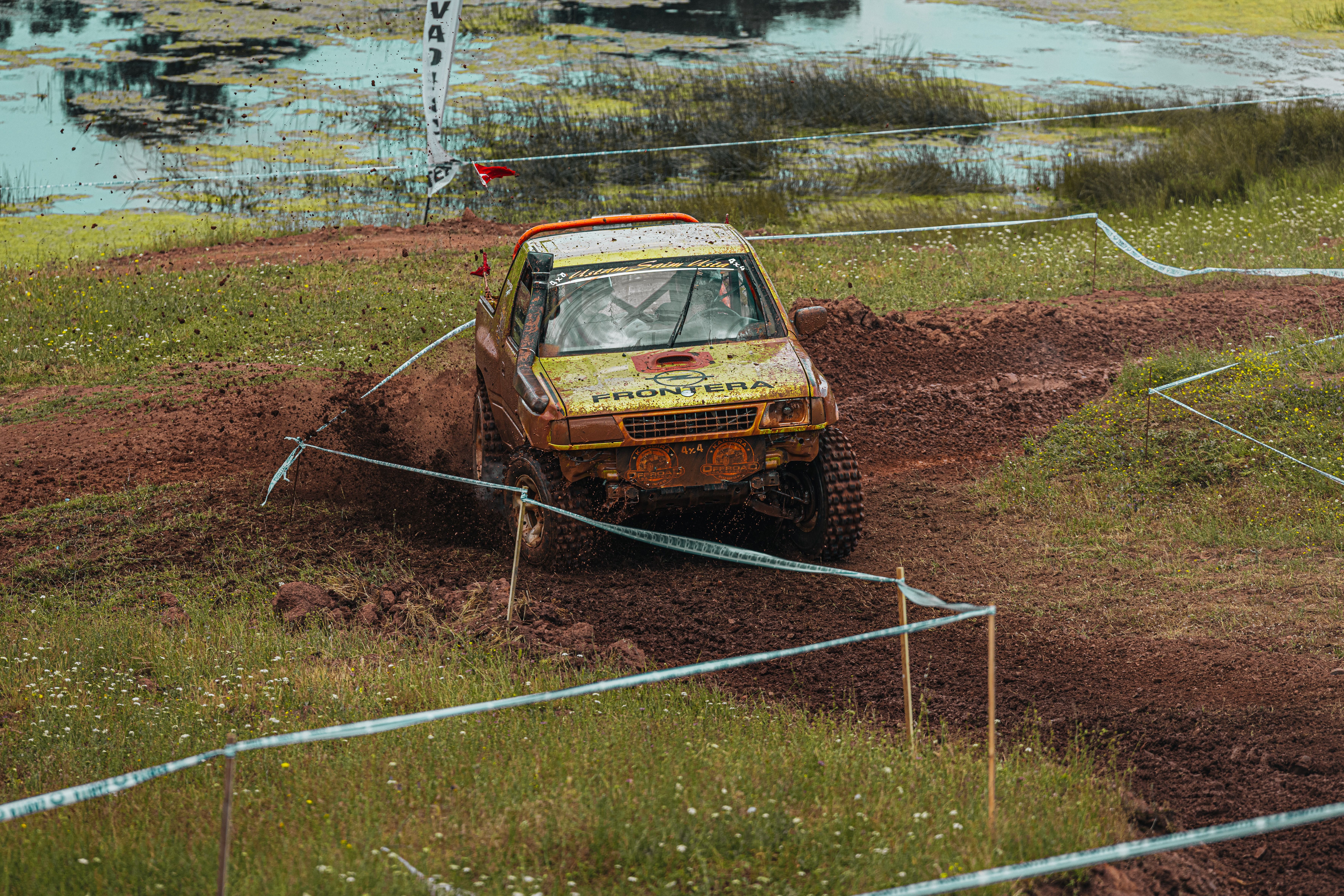 Off-road vehicle racing through a muddy course in an outdoor environment.