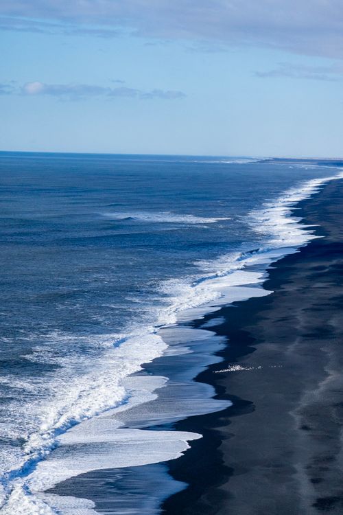 Free Stunning aerial view of a black sand beach with waves gently lapping the shore. Stock Photo