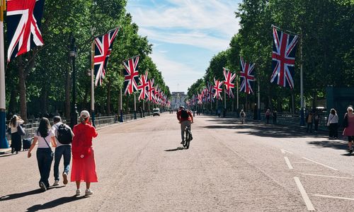 Free A cyclist rides down a street with Union Jack flags, heading towards Buckingham Palace in London on a sunny day. Stock Photo