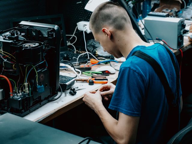 Technicien assis à un établi en train de réparer un appareil électronique dans un atelier