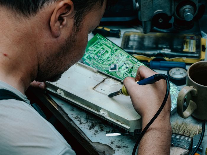 Close-up of a technician repairing an electronic board with a soldering iron