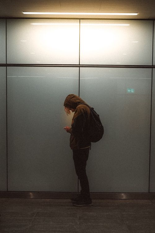 Free An individual stands in a moody Copenhagen subway, engaging with a smartphone. Stock Photo