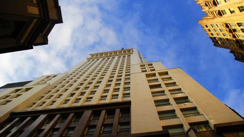 Free A towering skyscraper photographed from below against a vibrant blue sky with clouds. Stock Photo