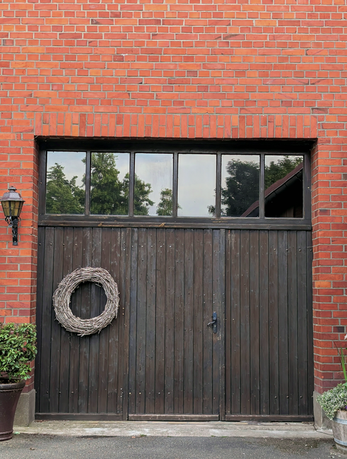 A rustic garage with wooden doors, brick walls, and a decorative wreath, perfect for home decor themes.