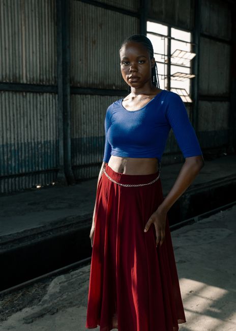 A young woman poses confidently indoors with industrial backdrop.