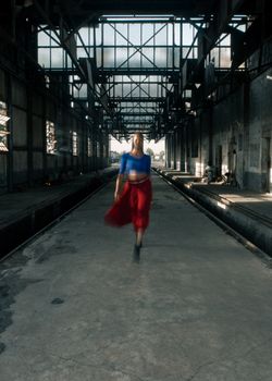 Blurred motion of woman dancing in a rustic industrial warehouse, wearing vibrant clothing.