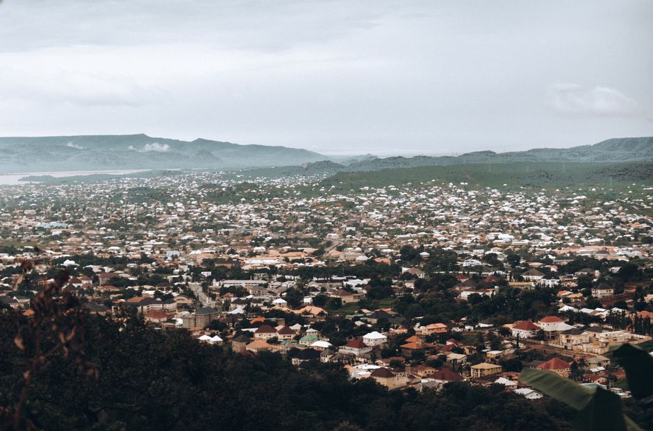 A panoramic view of a city surrounded by lush green hills under a cloudy sky.