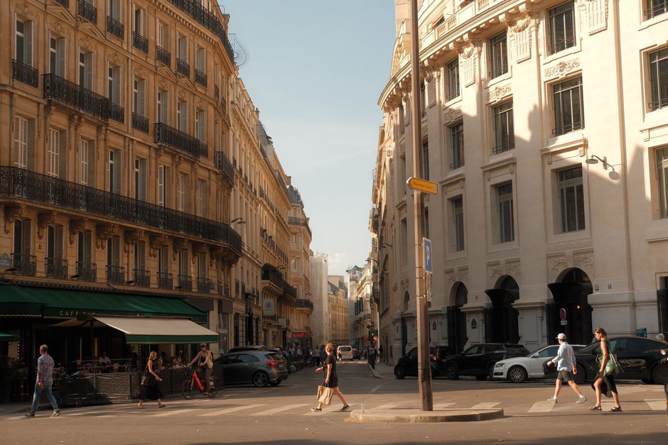 Sunlit Paris street with pedestrians and classic architecture, capturing vibrant city life.
