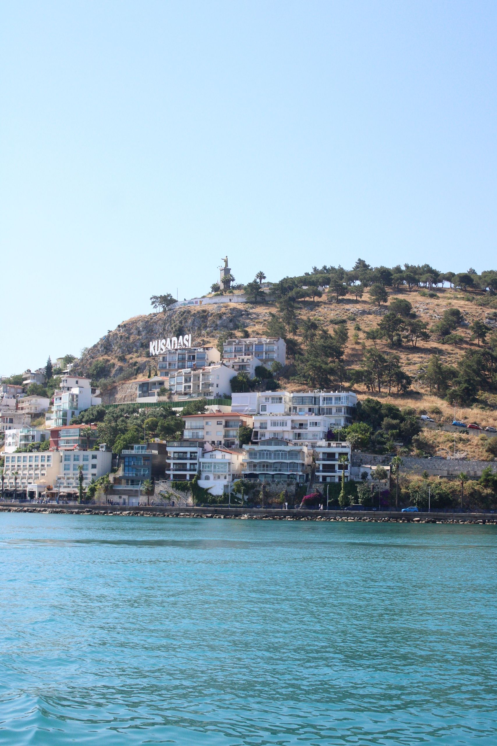 Beautiful coastal view of Kusadasi, Turkey with hillside and waterfront architecture under clear skies.