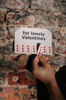 一只手从“献给孤独的情人节”海报上取下了心形标签，那海报贴在砖墙上