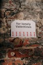 墙上有一块标志，上面写着“献给孤独的情人节”，还画着一颗红色的心，背景是崎岖不平的砖墙