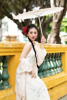 Elegant woman in traditional Vietnamese attire holding a parasol outdoors.