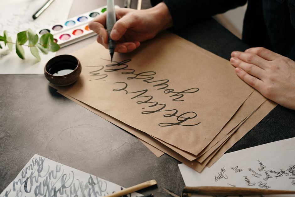 Close-up of hands creating calligraphy on craft paper with artistic tools