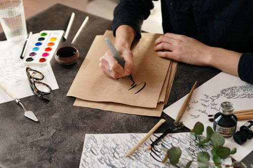 Free Creative workspace with calligraphy writing on parchment and art supplies. Stock Photo