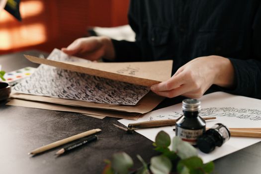 Close-up of calligraphy in progress with ink, pens, and paper on a desk. Art of hand lettering indoors.
