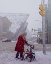 Senior woman using walker for moving alone through snowy pathway