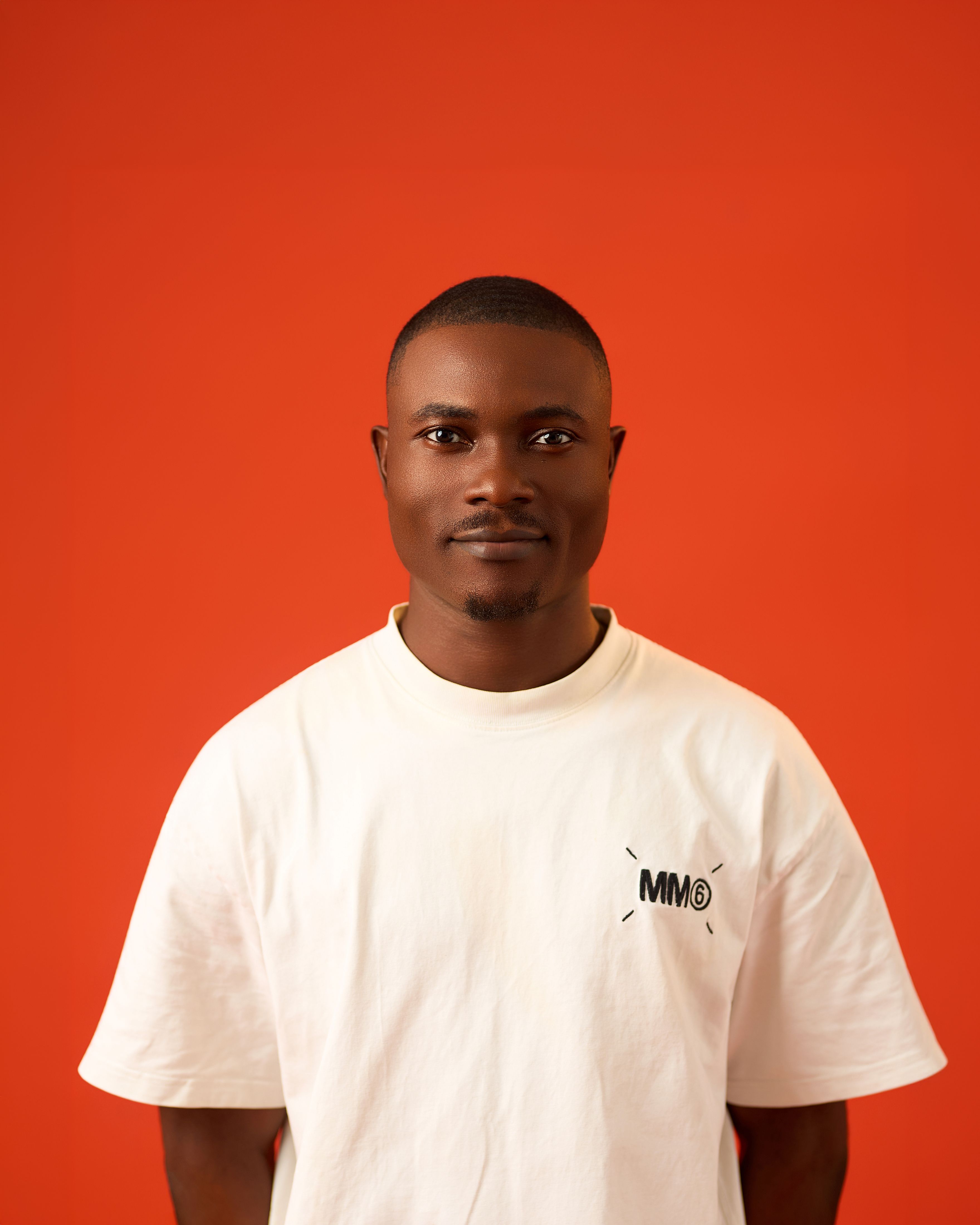 A confident young man in a white t-shirt stands against a vibrant orange background.