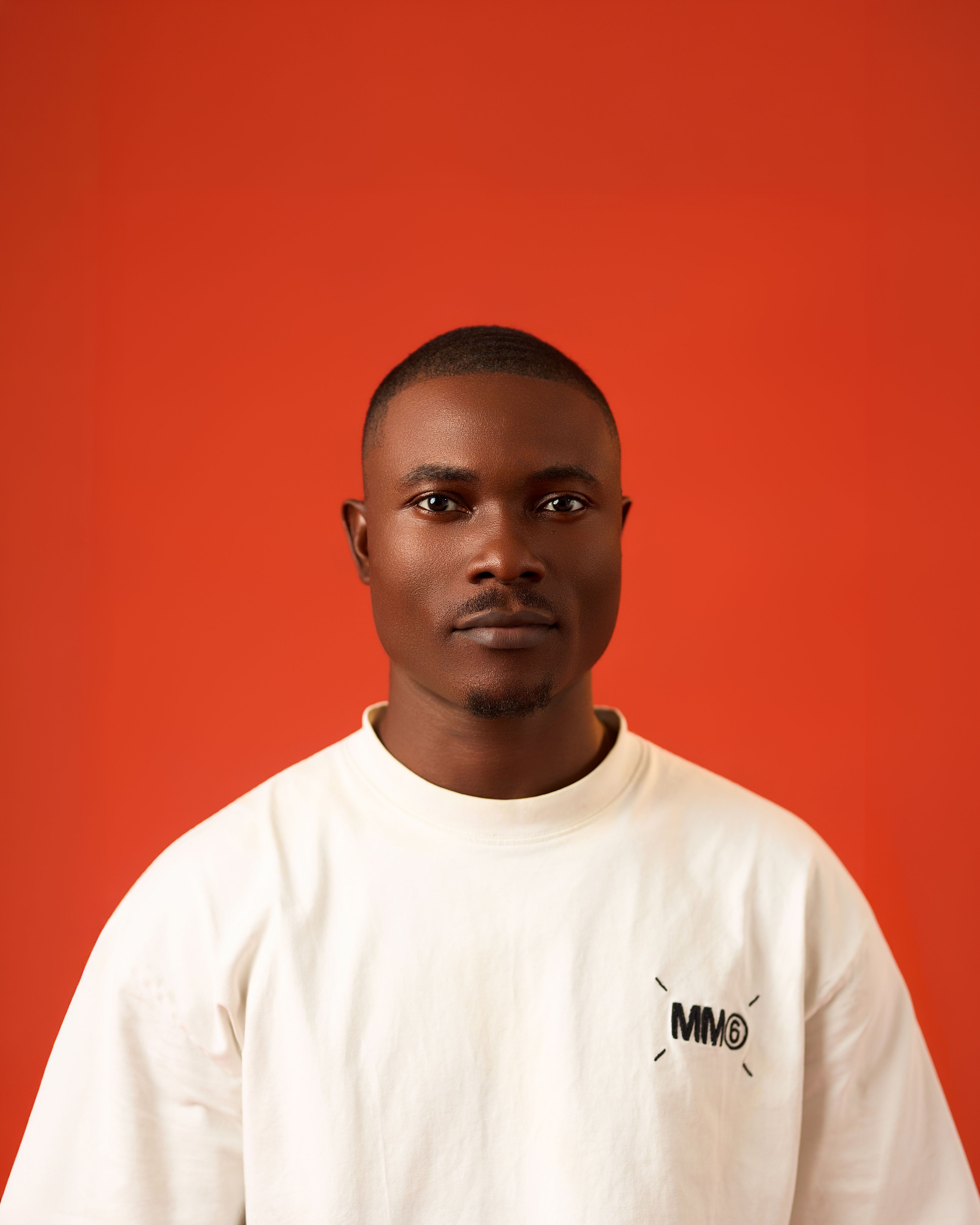 Studio portrait of a man standing against an orange backdrop, wearing a white shirt.