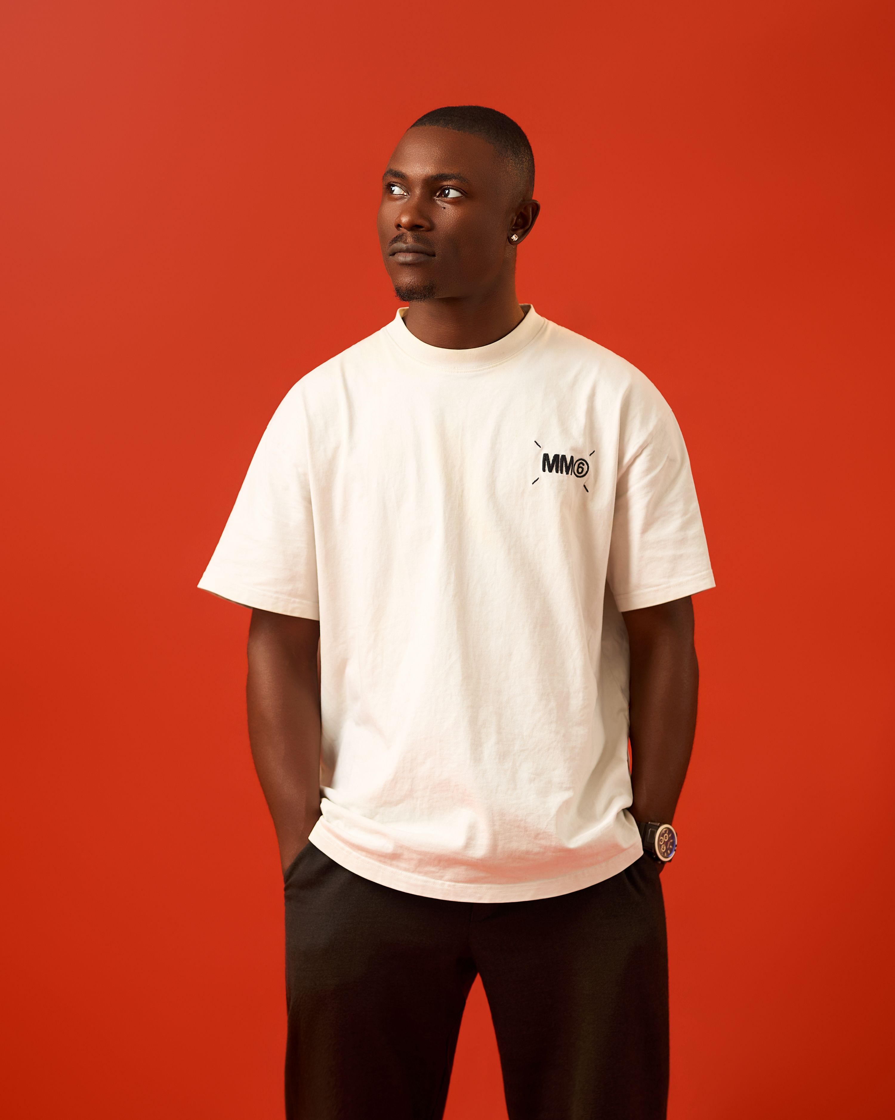 A thoughtful man poses against a vibrant red backdrop wearing a white T-shirt.