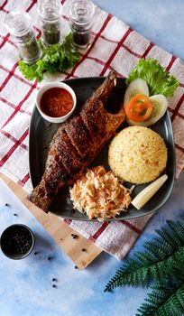 A flavorful grilled sea bass served with rice, salad, sauce, and garnish on a stylish plate.