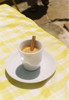 A cup of traditional Portuguese drink garnished with a cinnamon stick, set on a sunny table in Lisbon.