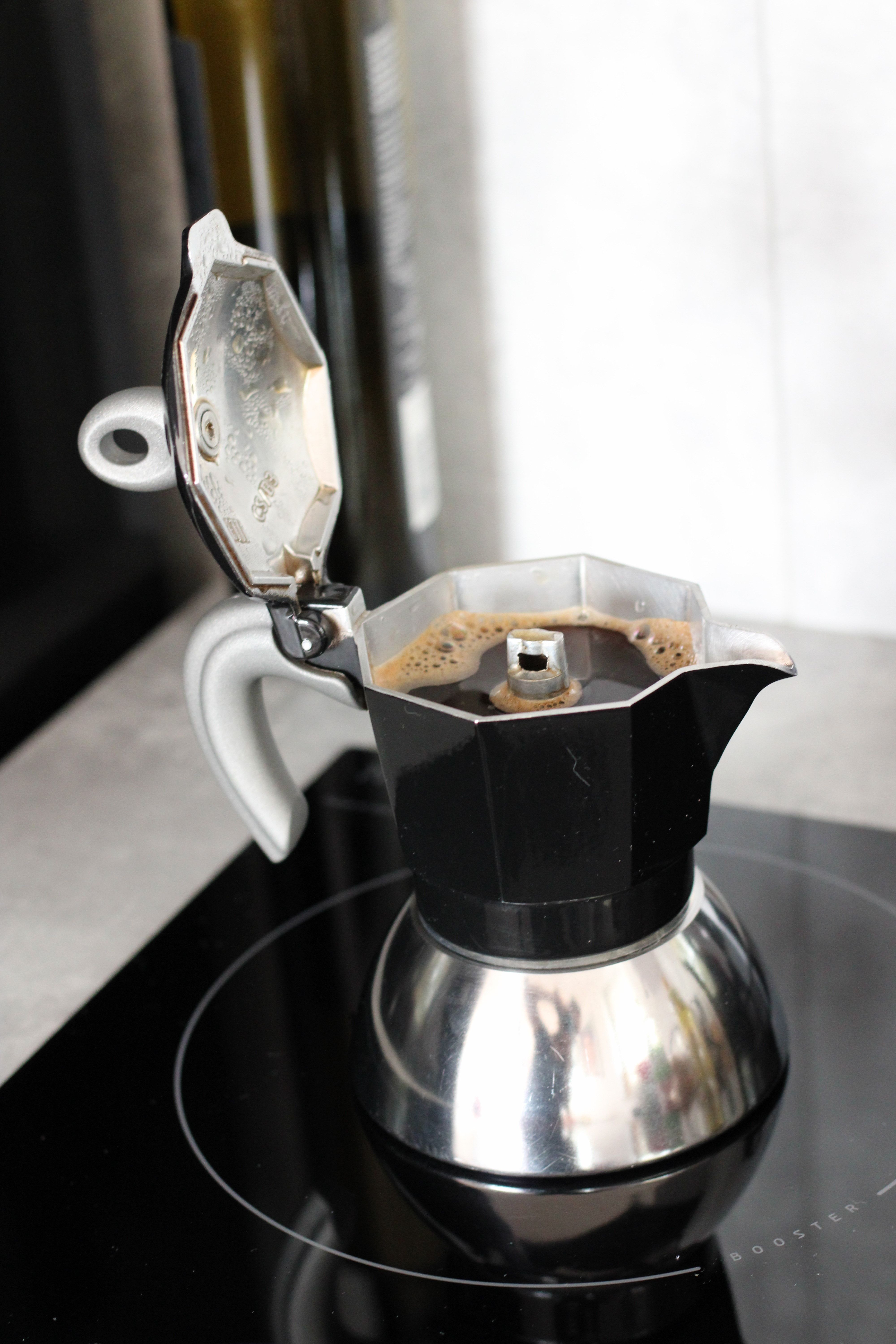 Close-up of traditional moka pot brewing coffee on an electric stove indoors.