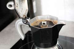 Close-up of traditional moka pot brewing coffee on an electric stove indoors.