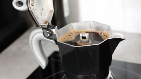 Close-up of traditional moka pot brewing coffee on an electric stove indoors.