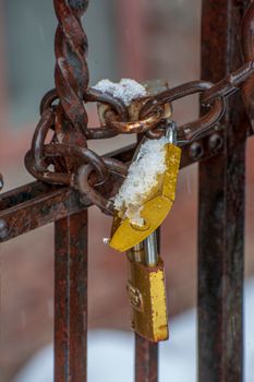 Close-up of a rusty chain with padlock covered in snow, depicting winter security.