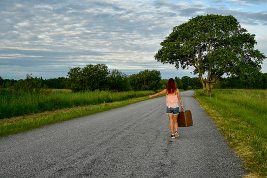 A woman with red hair hitchhiking in the Estonian countryside on a sunny summer day.