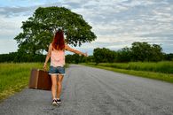 Young woman with suitcase hitchhiking on a scenic summer road in Kolga, Estonia.