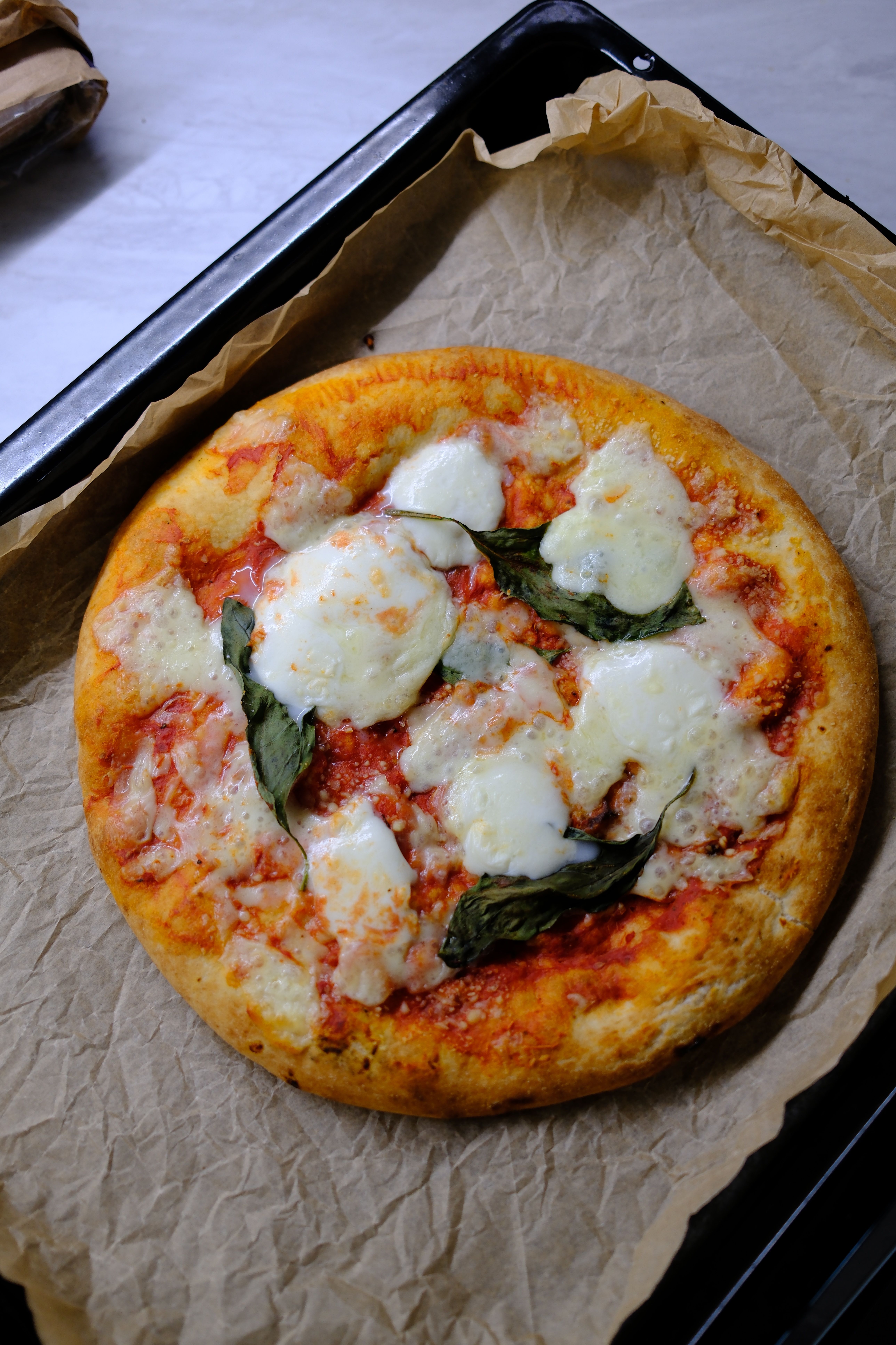 Freshly baked Margherita pizza with mozzarella and basil on parchment paper.