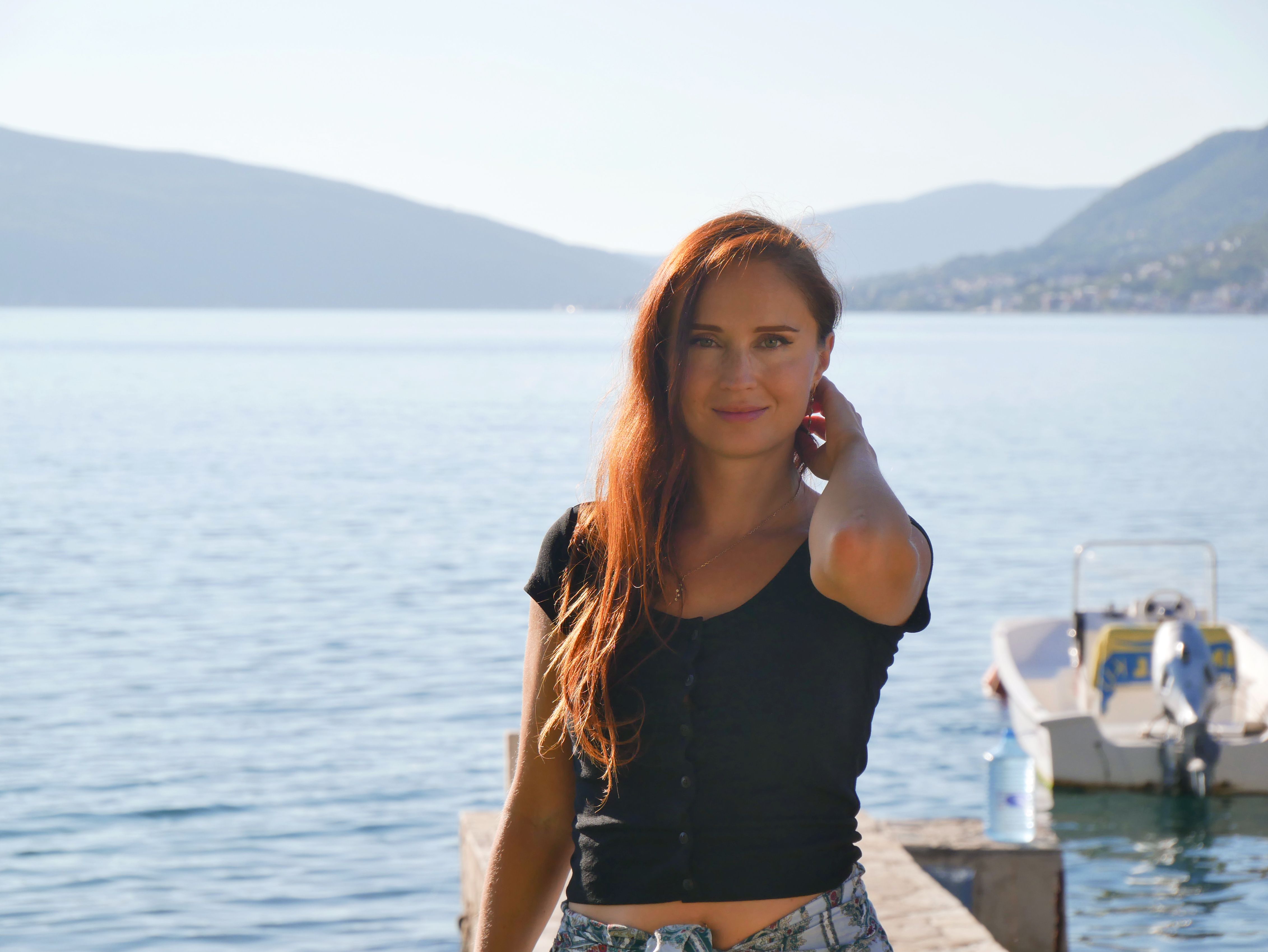 A young woman stands on a pier by the sea on a sunny day in Tivat, Montenegro.