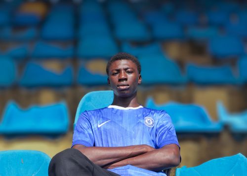 Free A young man wearing a blue jersey sits confidently in a stadium with blue seats in Nigeria. Stock Photo