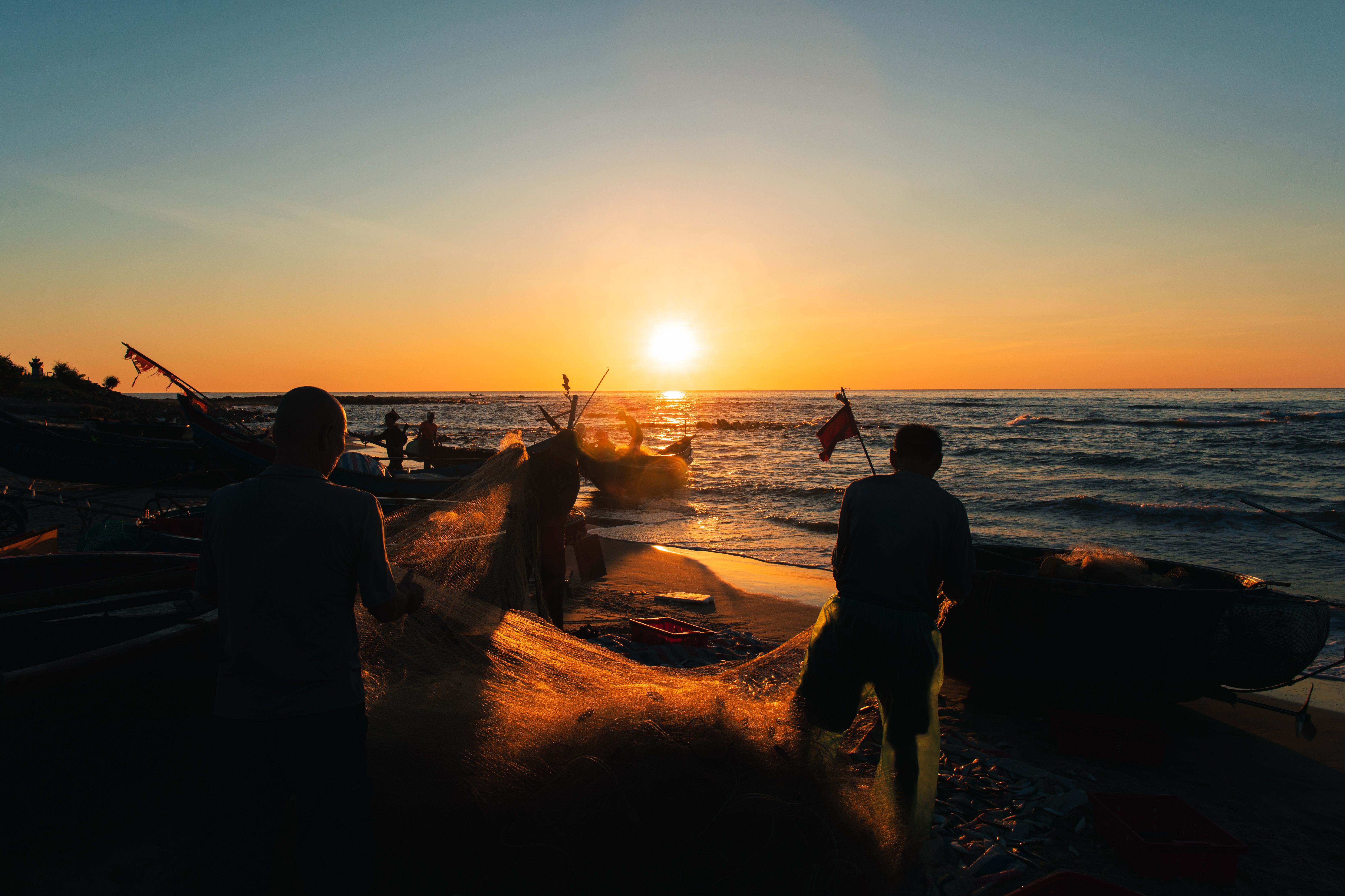 Silhouetted fishermen tending to nets on a Vietnam beach at sunrise.